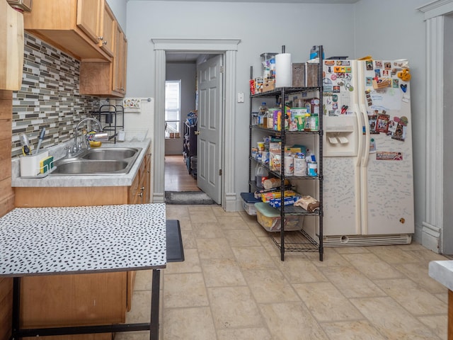 kitchen with white fridge with ice dispenser, light countertops, a sink, and backsplash