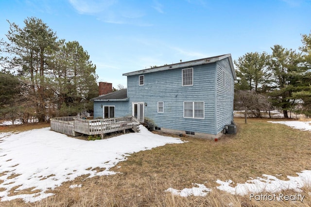 snow covered house with a chimney, a lawn, cooling unit, and a wooden deck