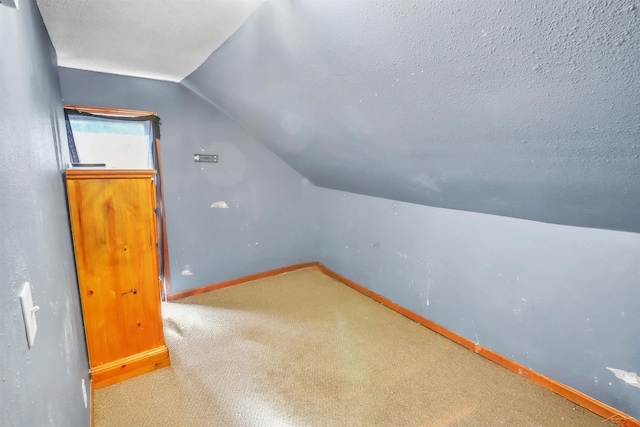 additional living space featuring a textured ceiling, vaulted ceiling, carpet flooring, and baseboards