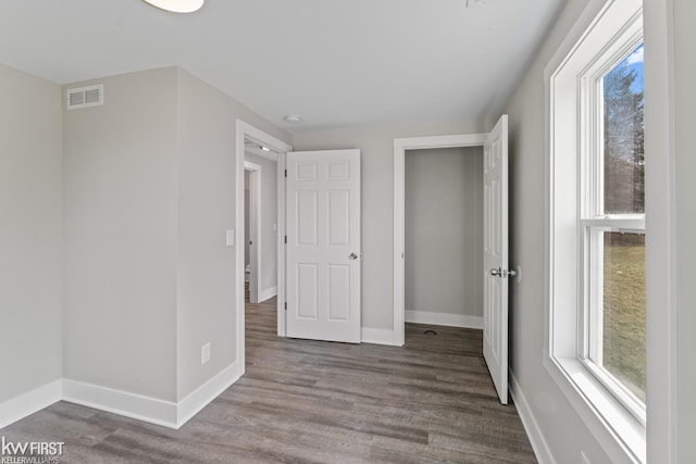 unfurnished bedroom featuring baseboards, multiple windows, visible vents, and wood finished floors