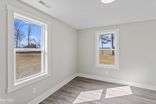 spare room with wood finished floors, visible vents, and baseboards