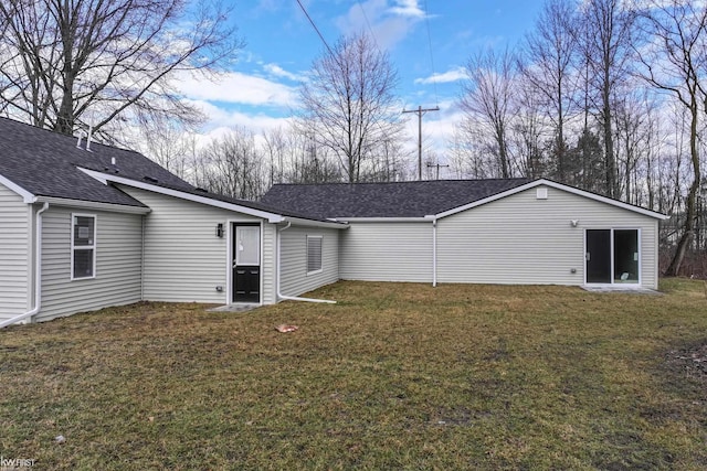 rear view of property featuring a shingled roof and a lawn