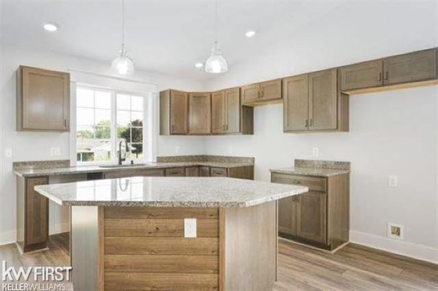 kitchen featuring light wood-style flooring, light stone counters, a center island, pendant lighting, and a sink