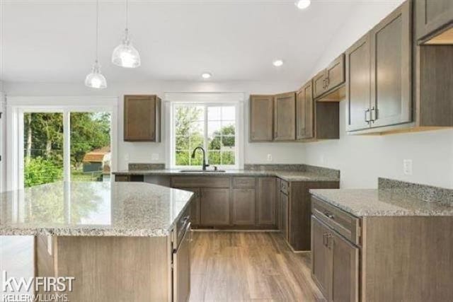 kitchen with light stone counters, a center island, light wood-style floors, and a sink