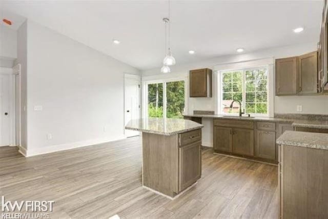 kitchen featuring light wood-style flooring, a sink, vaulted ceiling, a center island, and decorative light fixtures