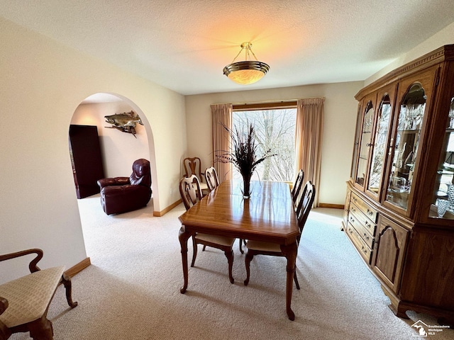 dining space with arched walkways, light carpet, a textured ceiling, and baseboards