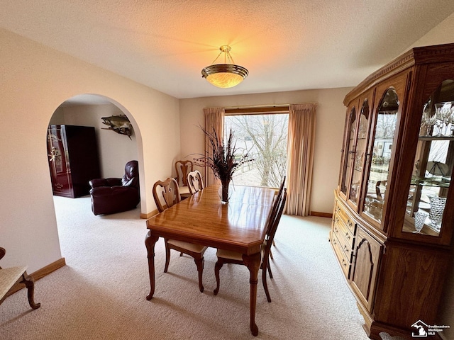 dining area with arched walkways, a textured ceiling, baseboards, and light colored carpet