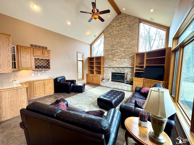 living area featuring a ceiling fan, beam ceiling, a fireplace, high vaulted ceiling, and indoor wet bar