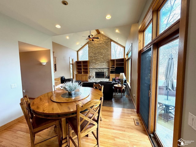 dining space featuring a fireplace, light wood finished floors, visible vents, high vaulted ceiling, and baseboards