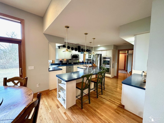 kitchen featuring dark countertops, a center island, stainless steel appliances, light wood-style floors, and a kitchen bar