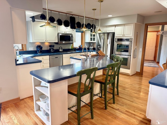 kitchen with stainless steel appliances, dark countertops, a sink, and light wood-style flooring