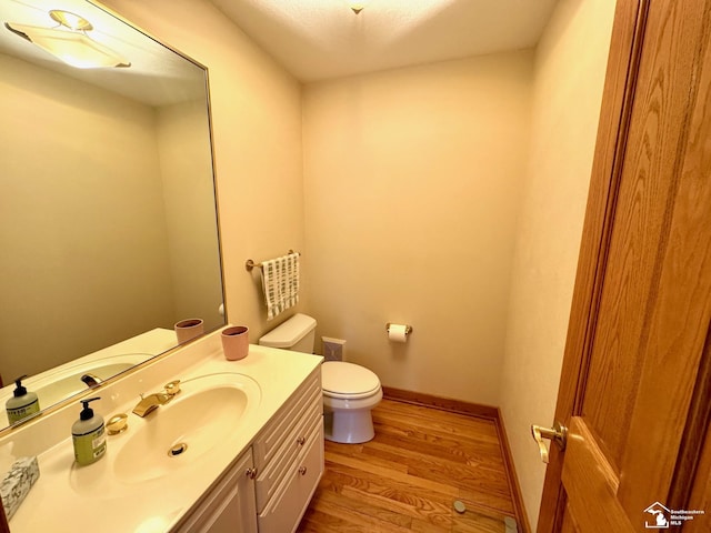 half bath with toilet, baseboards, wood finished floors, and vanity