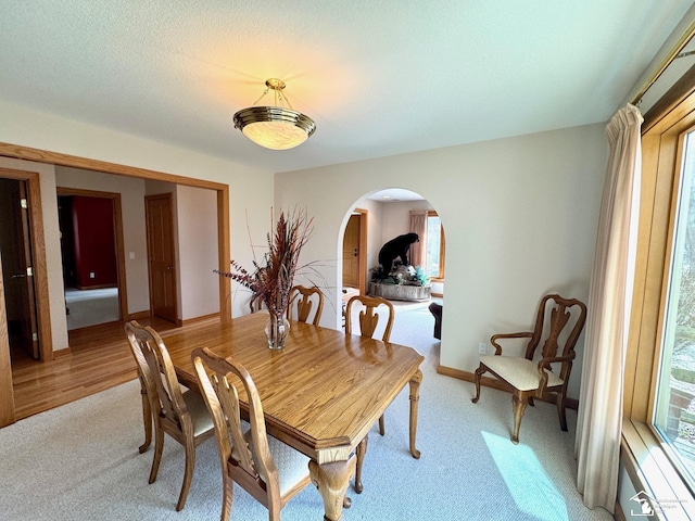 dining area with baseboards, arched walkways, a textured ceiling, and light colored carpet