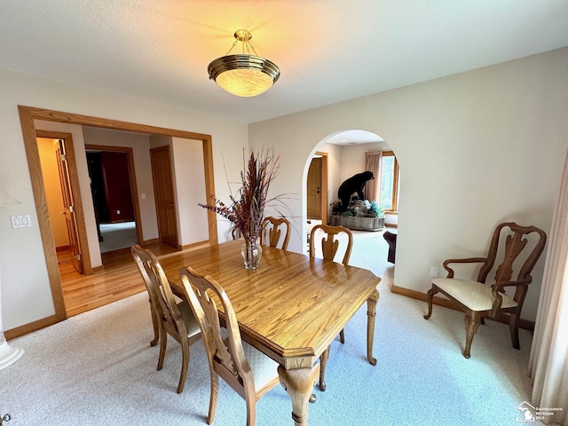 dining space featuring arched walkways, light colored carpet, and baseboards