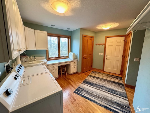 laundry room with cabinet space, light wood-style flooring, a sink, a textured ceiling, and independent washer and dryer