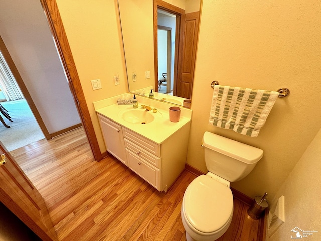 bathroom featuring toilet, baseboards, wood finished floors, and vanity