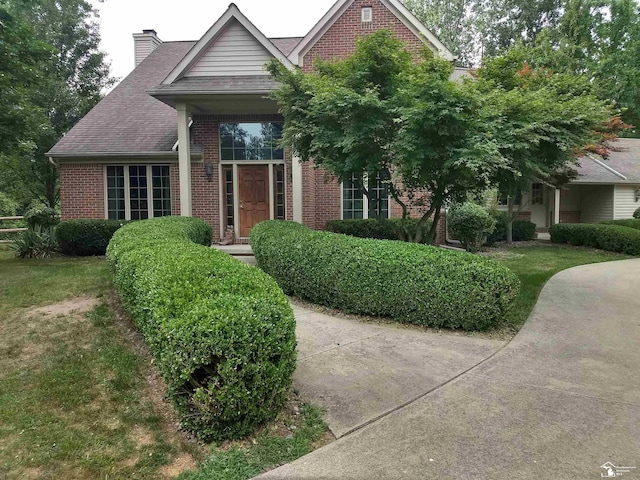 view of front of home with brick siding, a chimney, a shingled roof, and a front lawn