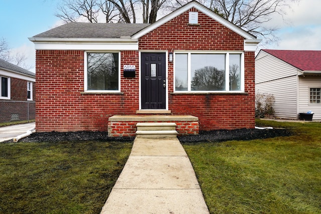 bungalow-style home featuring a shingled roof, a front yard, and brick siding