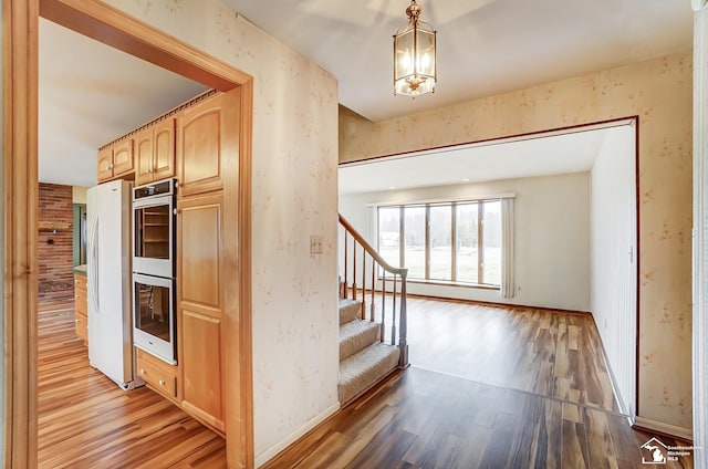 interior space with baseboards, freestanding refrigerator, light wood-type flooring, double oven, and light brown cabinets