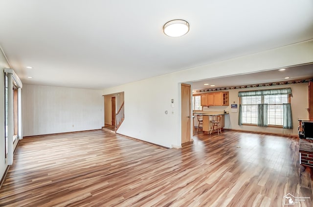 unfurnished living room with light wood-type flooring, recessed lighting, baseboards, and stairs