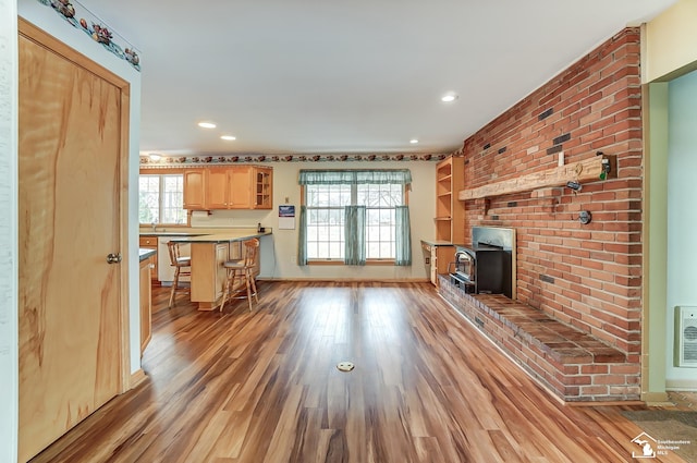 unfurnished living room with light wood-style floors, a wealth of natural light, a wood stove, and baseboards