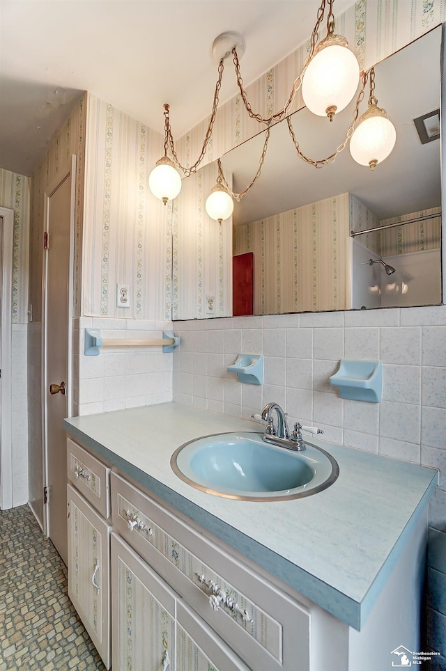 bathroom with tile walls, wainscoting, vanity, and wallpapered walls