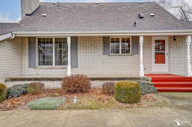 view of exterior entry with brick siding and roof with shingles