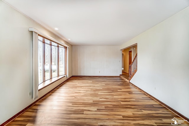 unfurnished room with stairway, light wood-style flooring, and baseboards