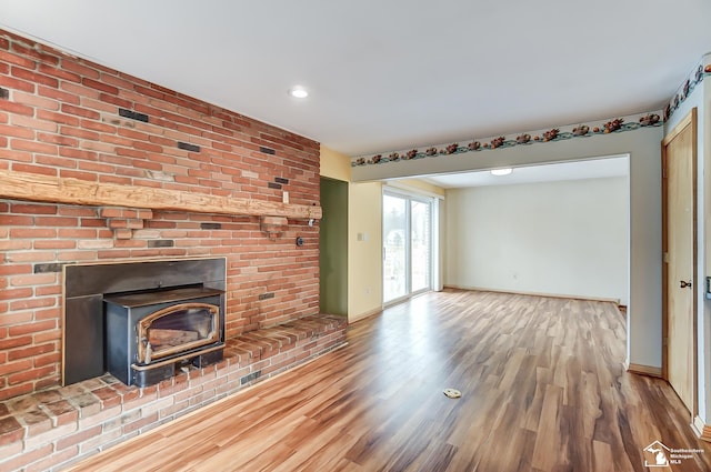 unfurnished living room featuring a wood stove, baseboards, and wood finished floors