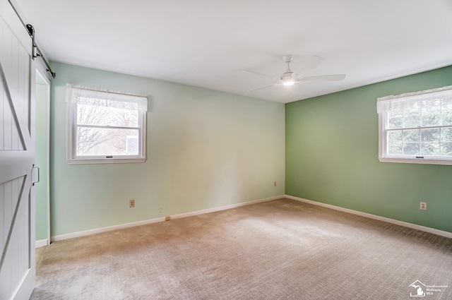 empty room featuring light colored carpet, ceiling fan, baseboards, and a barn door