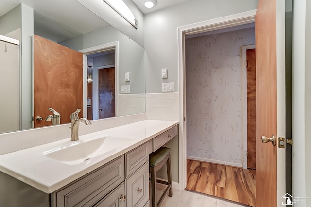 bathroom with wallpapered walls, baseboards, wood finished floors, and vanity