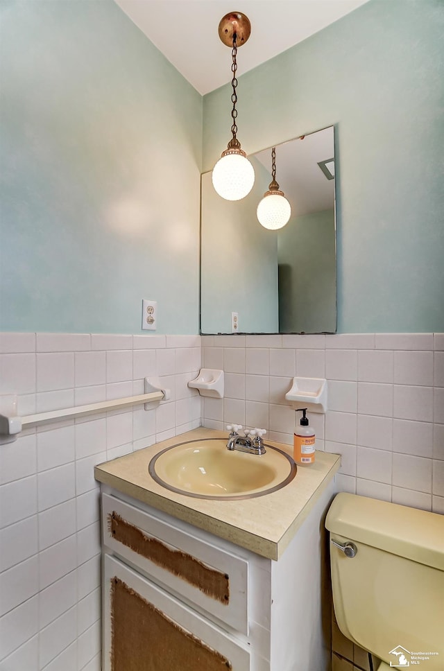 bathroom featuring toilet, a wainscoted wall, tile walls, and vanity