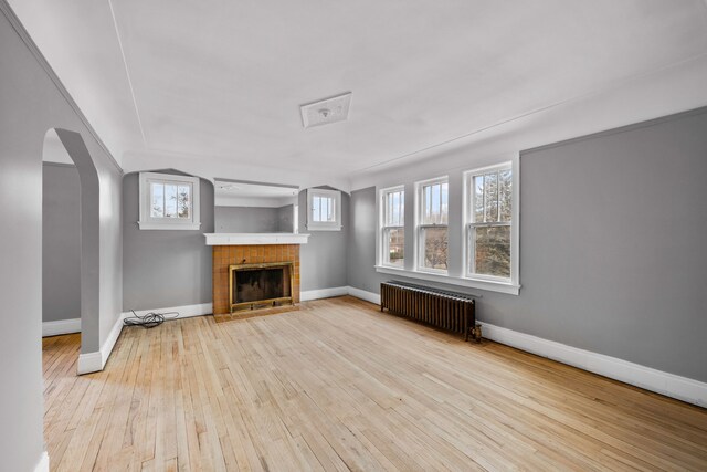2412 Cornell St, Dearborn, MI 48124 - unfurnished living room with arched walkways, radiator heating unit, a tile fireplace, baseboards, and hardwood / wood-style flooring