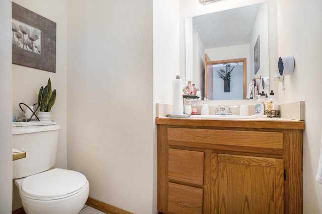 half bathroom featuring toilet, baseboards, and vanity