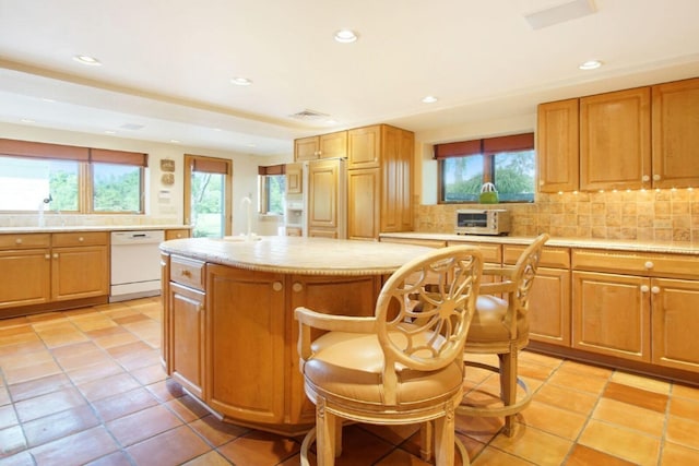 kitchen featuring backsplash, a center island, white dishwasher, light countertops, and a wealth of natural light