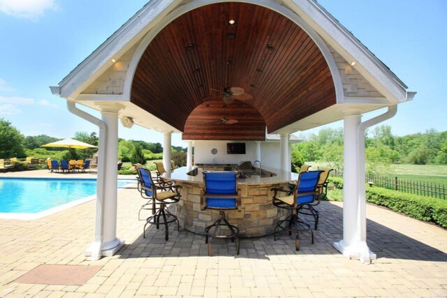 view of patio / terrace with a fenced in pool, a gazebo, fence, outdoor wet bar, and exterior kitchen