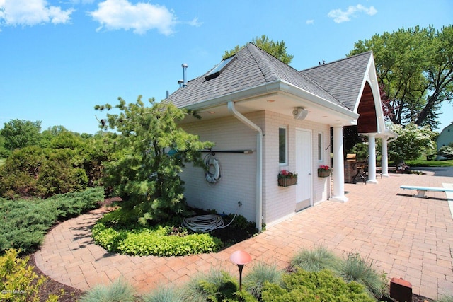 view of home's exterior with brick siding, a patio, and roof with shingles