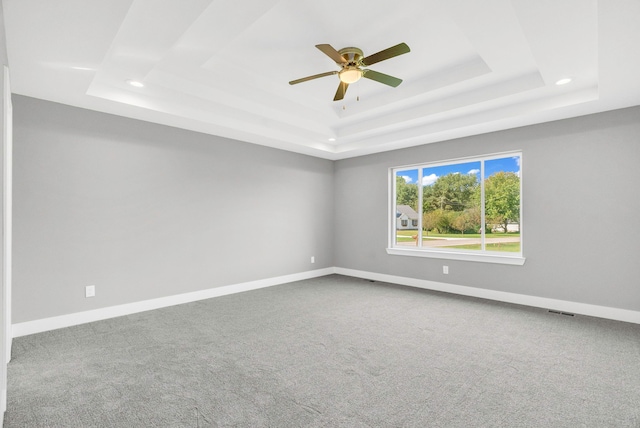 carpeted empty room with visible vents, baseboards, a raised ceiling, and a ceiling fan