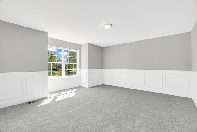 carpeted spare room featuring a wainscoted wall and visible vents