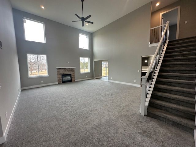 unfurnished living room featuring carpet, a fireplace, stairway, and baseboards