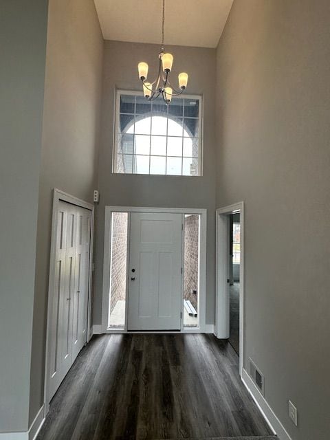 foyer entrance with dark wood-style floors, a notable chandelier, visible vents, a towering ceiling, and baseboards