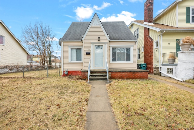 bungalow-style home with roof with shingles, a front yard, and fence