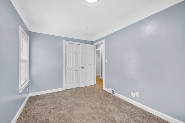 unfurnished bedroom with carpet, visible vents, baseboards, and a closet