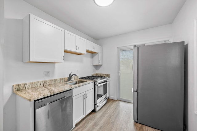 kitchen with light stone counters, appliances with stainless steel finishes, white cabinets, a sink, and light wood-type flooring