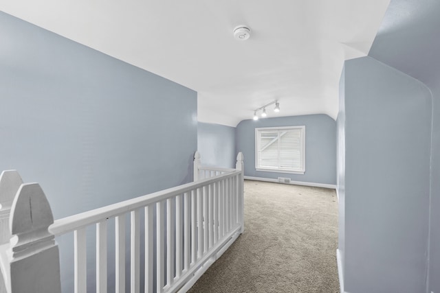 hall featuring carpet floors, an upstairs landing, baseboards, vaulted ceiling, and track lighting