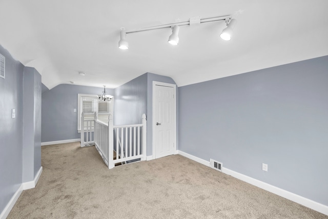 carpeted empty room featuring visible vents, baseboards, vaulted ceiling, and a chandelier