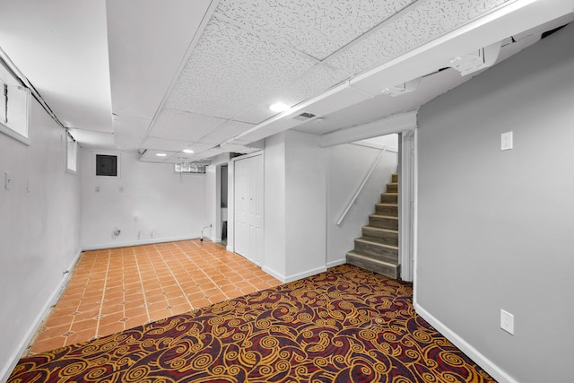 finished below grade area featuring stairs, visible vents, a drop ceiling, baseboards, and tile patterned floors