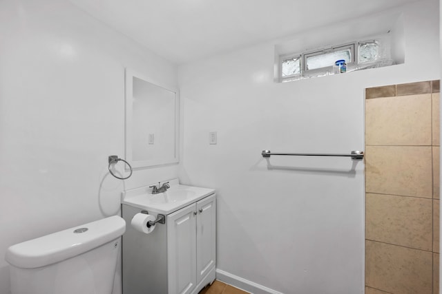 half bath featuring baseboards, vanity, and toilet