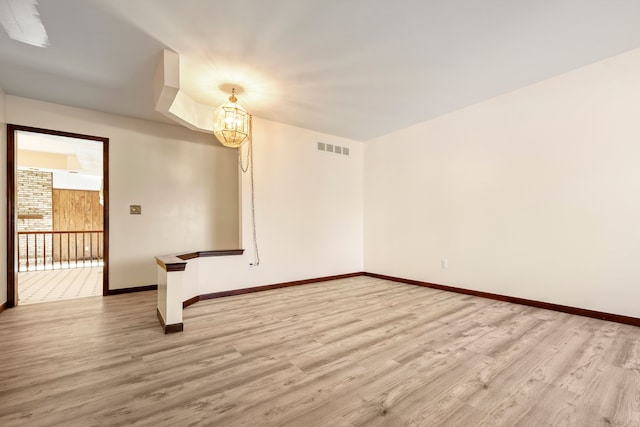 empty room with light wood-style floors, baseboards, visible vents, and a notable chandelier