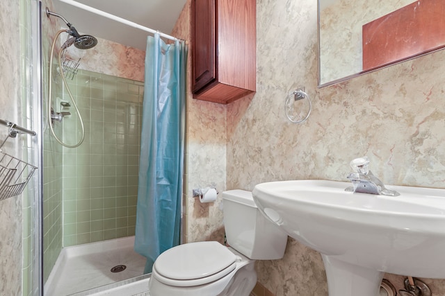 bathroom with toilet, a stall shower, a sink, and wallpapered walls